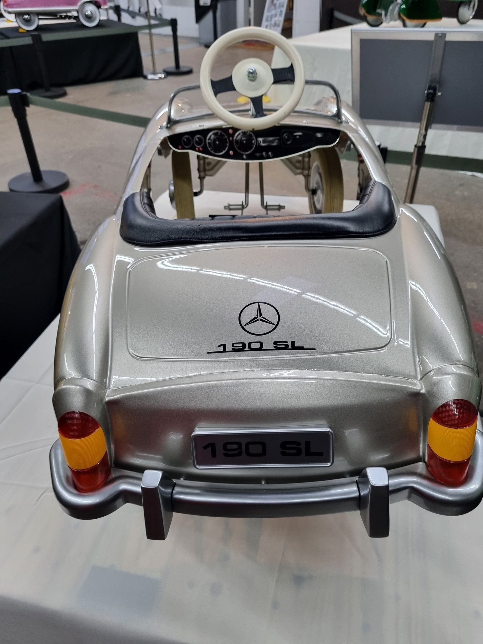 Auf einem Tisch steht ein silbernes Mercedes-Benz-Tretauto.